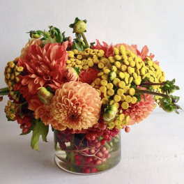 Low arrangement of orange dahlias and yellow button flowers in a clear glass vase
