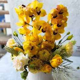 Yellow orchid arrangement in a white ribbed vase with small roses and textured blooms