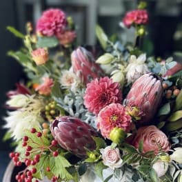 Mixed bouquet with pink blooms and protea in a white vase