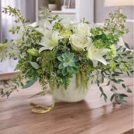 White roses and lilies in a ceramic vase with trailing greenery