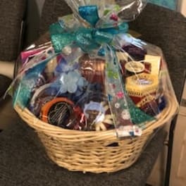 Gift basket wrapped in clear cellophane with assorted items and a teal bow