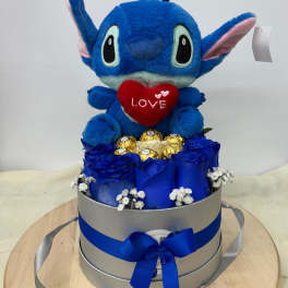 Blue plush character in a gift box with roses and chocolates