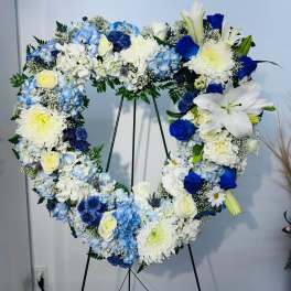 Heart-shaped floral wreath with blue, white, and yellow flowers on a stand
