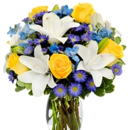 Bouquet of yellow roses, white lilies, and blue flowers in a glass vase
