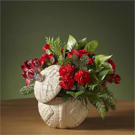 Red carnations in a woven basket with evergreen accents and a decorative ornament