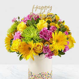 Bright mixed bouquet in a white vase with a gold "Happy" topper