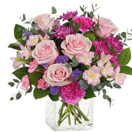 Pink roses and mixed blooms arranged in a clear glass vase