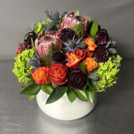 Bright mixed bouquet in a white round vase with orange roses and green hydrangeas