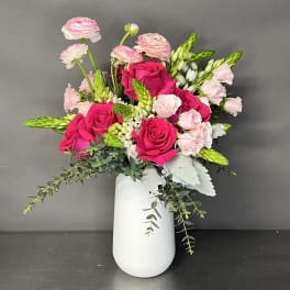 Pink roses and ranunculus in a white vase with trailing greenery