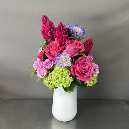 Bright pink roses and purple flowers arranged in a white vase