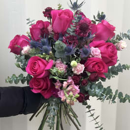 Hand-tied bouquet of hot pink roses with blue thistle and eucalyptus