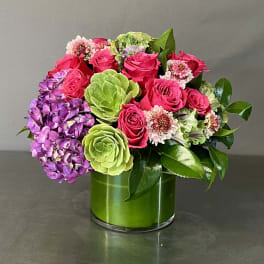 Pink roses and purple hydrangea in a green glass vase