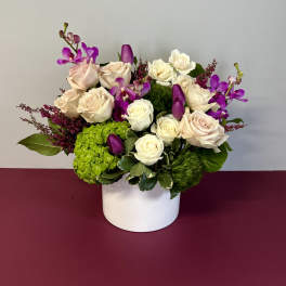 Bouquet of cream roses and purple orchids in a white vase