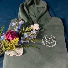 Green logo hoodie with a small colorful floral spray on a dark blue background
