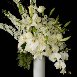 White floral arrangement in a tall white vase with orchids and lilies