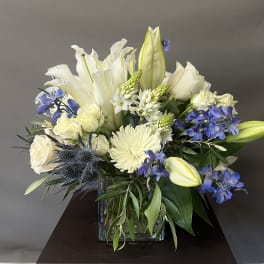 White lilies and roses with blue flowers in a square glass vase