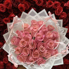 Handheld bouquet of pink roses wrapped in white paper with ribbons and pearl trim