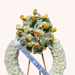 White floral funeral wreath with yellow roses and a ribbon on an easel