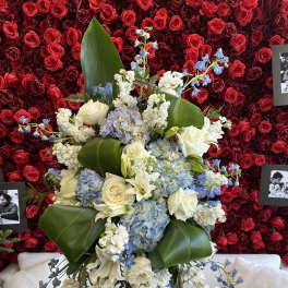 Large floral spray with white roses, blue blooms, and broad green leaves