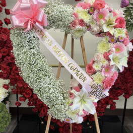 Heart-shaped floral wreath on an easel with pink and white flowers and a ribbon