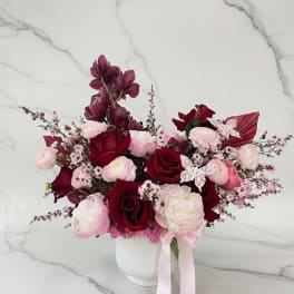 Bouquet of red and pink flowers in a white vase with a pink ribbon