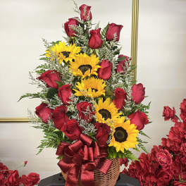 Basket arrangement of red roses and yellow sunflowers with a red ribbon
