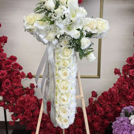 White floral cross arrangement on an easel with red rose backdrop