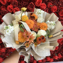 Bouquet of orange, white, and cream flowers wrapped in beige paper