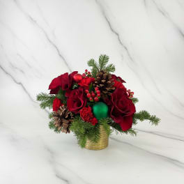 Red floral arrangement with pinecones and evergreen in a gold container