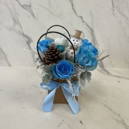 Blue roses in a small gift basket with a snowman ornament and pinecone