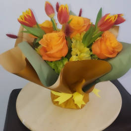 Bouquet of orange roses and red-yellow tulips wrapped in gold and green paper