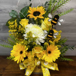 Yellow floral arrangement with sunflowers, roses, and a bee decoration