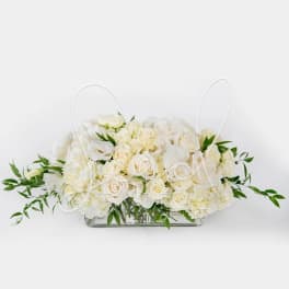 Low rectangular centerpiece of ivory roses and white blooms in a clear glass vase