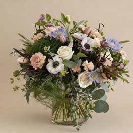 Loose pastel bouquet of roses, anemones, and carnations in a clear glass vase