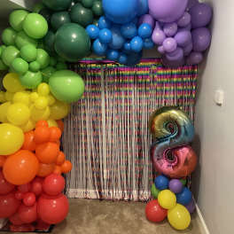Rainbow balloon arch with a metallic number 8 balloon and fringe backdrop