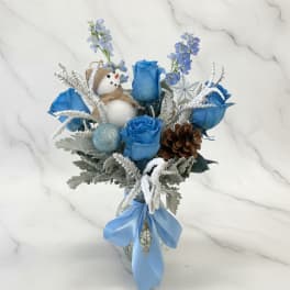 Blue rose bouquet with a snowman ornament and ribbon in a vase