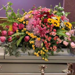 Large mixed floral spray on a casket with pink, yellow, and red blooms