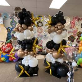 Two tall balloon columns in black, white, and gold with star balloons