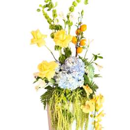 Tall floral arrangement with blue hydrangea and yellow orchids in a white vase
