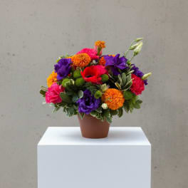 Bright mixed arrangement of orange, pink, purple, and red flowers in a small brown pot