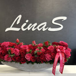 Long arrangement of red and pink roses in a gray container with a pink ribbon