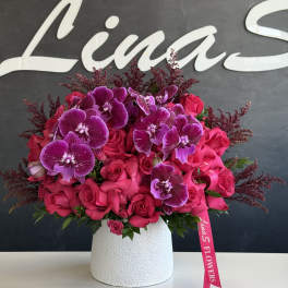 Pink roses and purple orchids arranged in a white vase