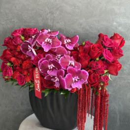 Red rose and purple orchid arrangement in a black vase