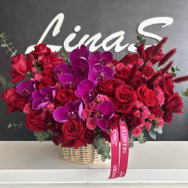 Basket arrangement of red roses and purple orchids with pink ribbon