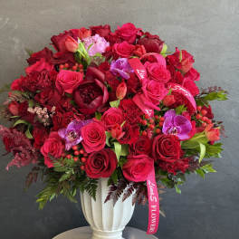 Large red rose arrangement in a white vase with pink orchids