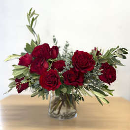 Red roses arranged in a clear glass vase with greenery