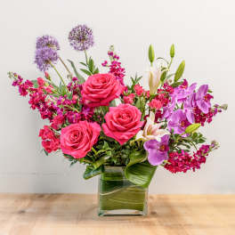 Pink roses and purple flowers arranged in a clear glass vase