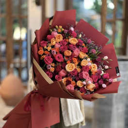 Large bouquet of pink, orange, and peach roses wrapped in burgundy paper