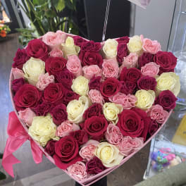 Heart-shaped box of pink, red, and cream roses tied with a pink ribbon