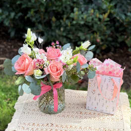 Pink rose bouquet in a glass vase beside a patterned gift bag